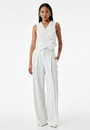 Top sans manches à volant avec des fines rayures blanches verticales, présentant des boutons dorés. Associé à un pantalon large à rayures, le tout en tissu léger.