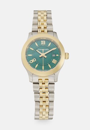 Zelta un sudraba tonēta nerūsējošā tērauda pulkstenis ar zaļo ciparnīcu, stundu atzīmēm un datuma funkciju. Tam ir teksturēta malu un saistīts aproce.