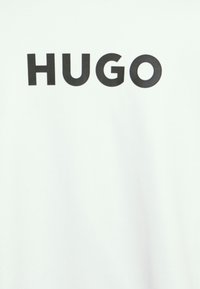 Bílý tričko s výrazným černým logem "HUGO" uprostřed. Vyrobeno z měkké tkaniny s hladkou texturou.