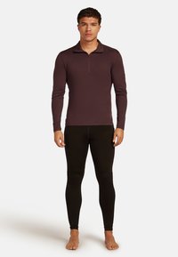 Camiseta de manga larga con cremallera en tela morada oscura; combinada con leggings negros. Textura suave, diseño ajustado. Presenta detalles de costura mínimos.
