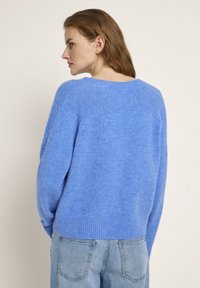 Blauer Strickpullover mit geripptem Saum und Bündchen, der eine entspannte Passform und weiche Textur bietet. Der Rücken hat einen abgerundeten Ausschnitt und minimale Nähte.