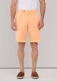 Pantalones cortos de algodón color durazno con botón en la parte delantera, bolsillos planos y dobladillos. Llevados con zapatos de ante marrón tipo slip-on.