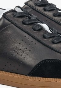 Zwarte leren sneakers met geperforeerde details, textuur van zwart suède op de accenten, platte zwarte veters en tan rubberen zolen. Eenvoudig ontwerp.