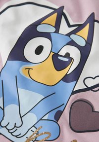 Tecknet figur af en blå hund med gule detaljer, omridset i sort. Baggrunden har hjerter og en pink bund med guldglitterdetaljer.