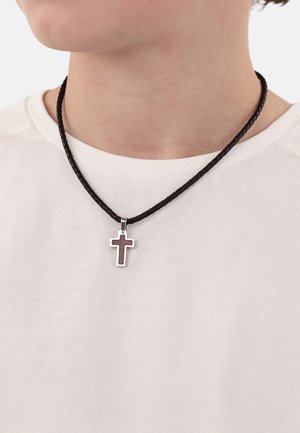 Schwarzes, geflochtenes Lederhalsband mit einem silbernen Kreuzanhänger und dezentem tiefrotem Einlegeschild, getragen über einem weißen Hemd.