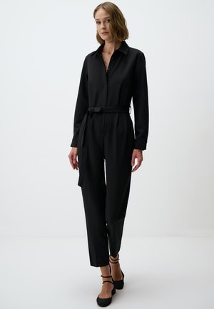 Jumpsuit nero a maniche lunghe con collo a camicia, chiusura frontale a bottoni, cintura legata in vita e silhouette a gamba dritta.