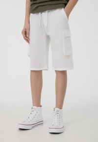 Pantaloni cargo bianchi in lino con due tasche laterali, una cintura con cordoncino e una linea dritta. Abbinati a sneaker alte bianche.