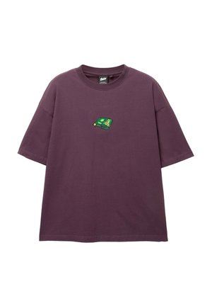 Tricou din bumbac mov, cu o croială lejeră, având un mic patch brodat în verde și galben pe piept. Mâneci scurte și decolteu rotund.