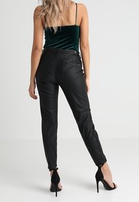 Černé kalhoty z umělé kůže s úzkým střihem, vysokým pasem a zadními kapsami. Stajlováno s zeleným sametovým topem a černými lodičkami na vysokém podpatku.