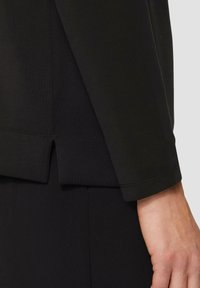 Schwarzes Langarmoberteil mit gerippter Textur, das an dem Saum einen seitlichen Schlitz und ein glattes Finish an den Ärmeln aufweist.