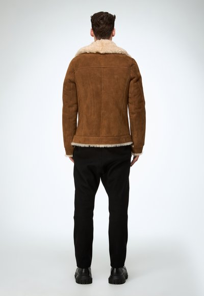 Braune Wildlederjacke mit einem Lammfellkragen, tailliertem Schnitt und sichtbaren Nähten. Kombinieren Sie sie mit schwarzen Hosen und klobigen schwarzen Stiefeln.