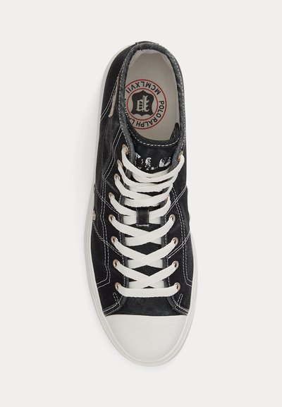 Black canvas sneaker with white rubber toe cap, white laces, and visible logo on the beige insole, viewed from above on a white background.