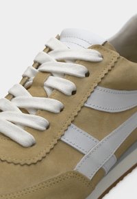 Μπεζ αθλητικό παπούτσι από σουέντ με λευκές δερμάτινες ρίγες και κορδόνια, υφασμάτινη υφή, οδοντωτή ραφή και καουτσούκ σόλα.