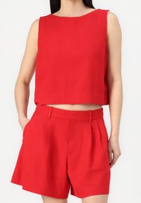 Haut rouge court sans manches associé à un short rouge taille haute. Fabriqué dans un tissu lisse avec un design épuré et boxy, et de légères plis.