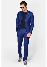 Niebieski garnitur w wzory o dopasowanym kroju, zestawiony z czarnym t-shirtem i szarymi trampkami. Garnitur ma klapę w kształcie notcha oraz subtelny wzór w kraty.