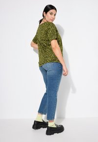 Camiseta de manga corta verde oliva con manchas de leopardo en negro y amarillo, combinada con jeans rectos de pierna clara y zapatos de plataforma negros con tachuelas.