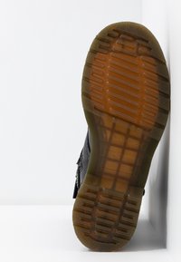 Semelle de chaussure noire avec une traction en caoutchouc texturé ; présente un motif en relief et des bordures transparentes marron. Conception à bout plat et arrondi.