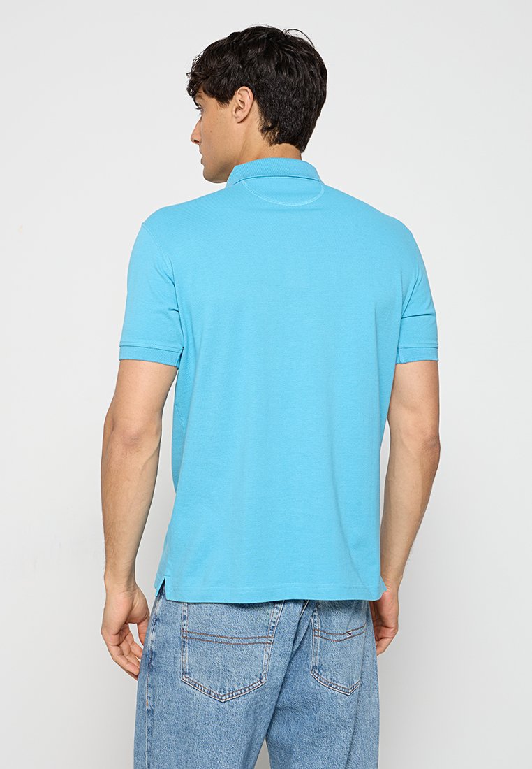 Lichtblauwe polo met een klassieke kraag, korte mouwen en een rechte zoom. De stof lijkt zacht met een gladde textuur.