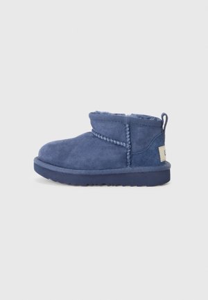 Bottine bleu en daim à la cheville avec doublure douce, détails de couture tressée, languette à l'arrière et semelle texturée sur un fond clair uni.