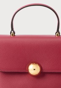 Borsa a mano in pelle rossa con superficie lavorata e manico corto. Presenta una chiusura rotonda dorata con la scritta "Furla" incisa. Design minimalista.