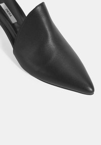 Mule en cuir noir à bout pointu avec un dessus élégant, texture lisse et design minimaliste. Dotée d'un talon moyen pour plus de hauteur.