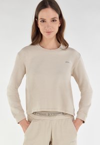 Felpa corta beige con maniche lunghe, colletto a coste e discreto dettaglio del logo. Tessuto morbido, vestibilità casual, abbinata a pantaloni coordinati.