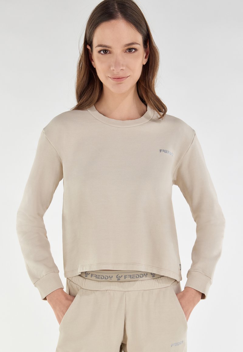 Felpa corta beige con maniche lunghe, colletto a coste e discreto dettaglio del logo. Tessuto morbido, vestibilità casual, abbinata a pantaloni coordinati.