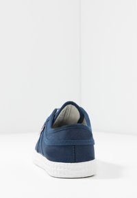 Marineblaue Leinensneaker mit einer strukturierten weißen Gummisohle, einem Rückenteiler und einem kleinen Logodetail an der Seite. Einfaches Design und klare Linien.