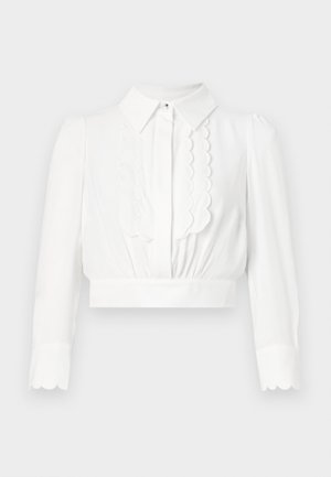 White cropped blouse with a collar, scalloped detailing down the front, and long sleeves with scalloped cuffs. Smooth, lightweight fabric.