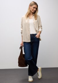 Camicia beige a bottoni, canotta bianca, jeans a gamba larga blu scuro, sneakers bianche, borsa in suede marrone. Design semplice, look casual.