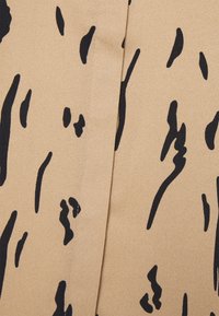 Tissu beige avec des formes verticales noires abstraites et irrégulières, avec un détail de couture centrale.