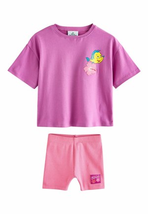 Toddler wearing pink cap, purple t-shirt with fish graphic, pink shorts, white socks, and pink sneakers, standing and looking up.