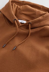 Sudadera marrón acanalada con bolsillo frontal, cordones y un corte relajado. Fabricada en algodón con un acabado texturizado.
