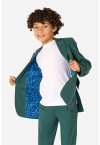 Giacca e pantaloni verde, con una fodera a motivi geometrici blu, abbinati a una t-shirt bianca semplice. Tessuto testurizzato con vestibilità su misura.
