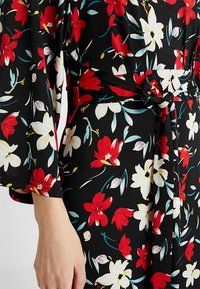 Blommig klänning med svart bakgrund och livfulla röda och vita blommor, långa ärmar, knytning i midjan och mjukt, flödande tyg.