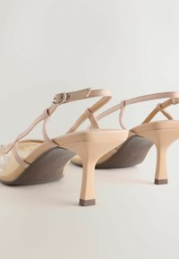 Sandale cu toc înalt, bej, cu un design elegant, prevăzute cu o baretă subțire la gleznă și un toc modelat, de culoare deschisă. Detaliu floral în zona degetelor.