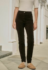 Zwarte corduroy broek met een slim fit, voorzien van voorzakken en een knoopsluiting, gecombineerd met tan moccasin-stijl schoenen.