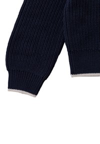 Ärmel eines marineblauen Strickpullovers mit geripptem Muster und kontrastierendem, hellfarbigem Besatz an der Manschette. Präzises Strickmuster ist durchgehend sichtbar.
