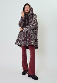 Kurtka parka w panterkę, wodoodporna, z kapturem, z zamkiem błyskawicznym i elastycznymi mankietami, połączona z burgundowymi spodniami dzwonami oraz masywnymi czarnymi butami.