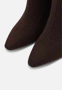 Bottes ankle en tissu côtelé marron avec des orteils pointus et une silhouette élégante. La finition texturée améliore la profondeur visuelle et le détail.