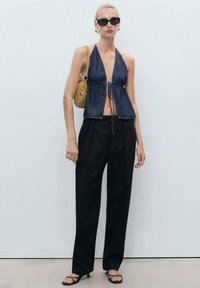 Denim zkrácený halter top s nastavitelným zavíráním na mašli, v kombinaci s černými plisovanými kalhotami a černými sandály na podpatku. Žlutá kabelka s kulatými prvky.
