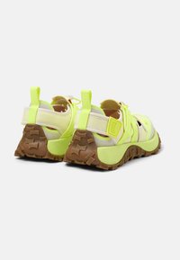 Sneakers con una toma verde lime, cinturini beige e una suola in gomma marrone testurizzata. Presentano linguette per il tiro e un design a ritaglio per la ventilazione.