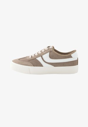 Niskie beżowe zamszowe sneakersy z białymi zygzakowatymi paskami po bokach, białymi sznurowadłami i grubą białą gumową podeszwą.
