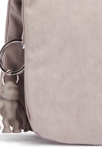 Grijze stoffen tas met een gestructureerd oppervlak, voorzien van een metalen sleutelhanger waaraan een klein grijs figuurtje hangt. Compact en eenvoudig ontwerp.