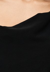 Κοντινό πλάνο του ώμου και του πάνω μέρους του στήθους ενός ατόμου που φοράει μαύρο ρούχο με ακάλυπτους ώμους πάνω στο δέρμα.