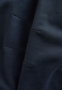 Laivastonsininen, teksturoitu kangas, jossa on pehmeä viimeistely. Kangas sisältää näkyvät saumat ja laskokset, mikä korostaa materiaalin paksuutta ja laskeutuvuutta.