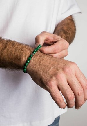 Žalias karoliukų apyrankė, pagaminta iš lygių apvalių malachito akmenų, tarp karoliukų yra sidabrinis akcentas. Apykaklė uždėta ant riešo, kur matosi plaukai.