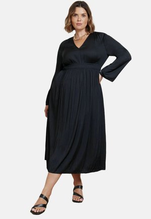 Zwarte geplooide jurk met lange mouwen, een V-halslijn en een elastische taille; gecombineerd met zwarte strepen sandalen. Gladde stoftextuur.