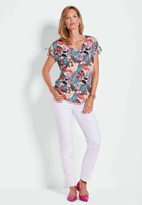 Bloemmotief top met korte mouwen en strikaccenten, gecombineerd met witte skinny jeans en roze hoge hakken.