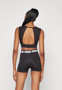 Top corto atlético negro con diseño de espalda con ojal y banda con logotipo, combinado con pantalones cortos negros ceñidos que cuentan con una cinturilla en contraste.